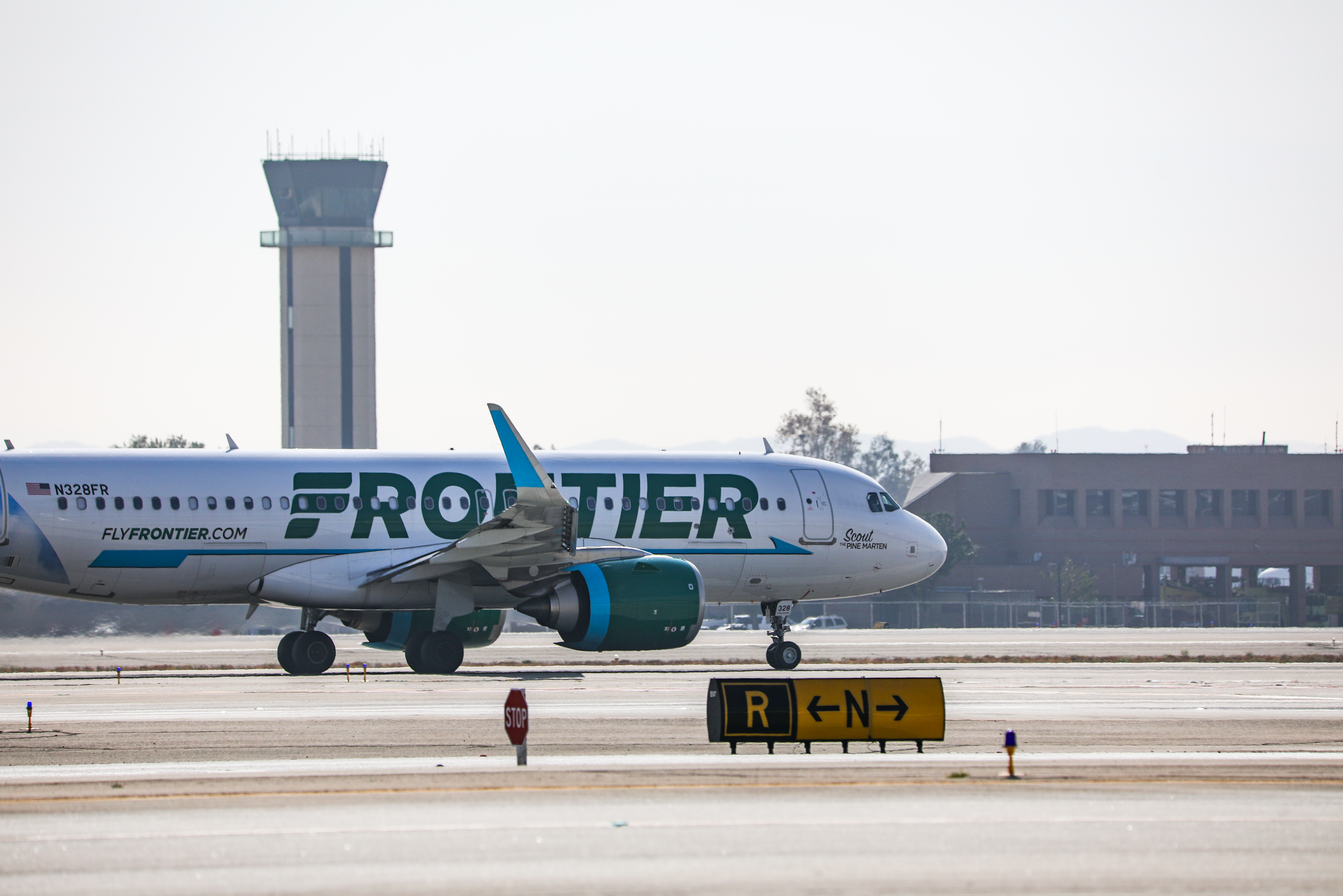 A Frontier Airlines plane with teal tail fin taxiing on airport runway.