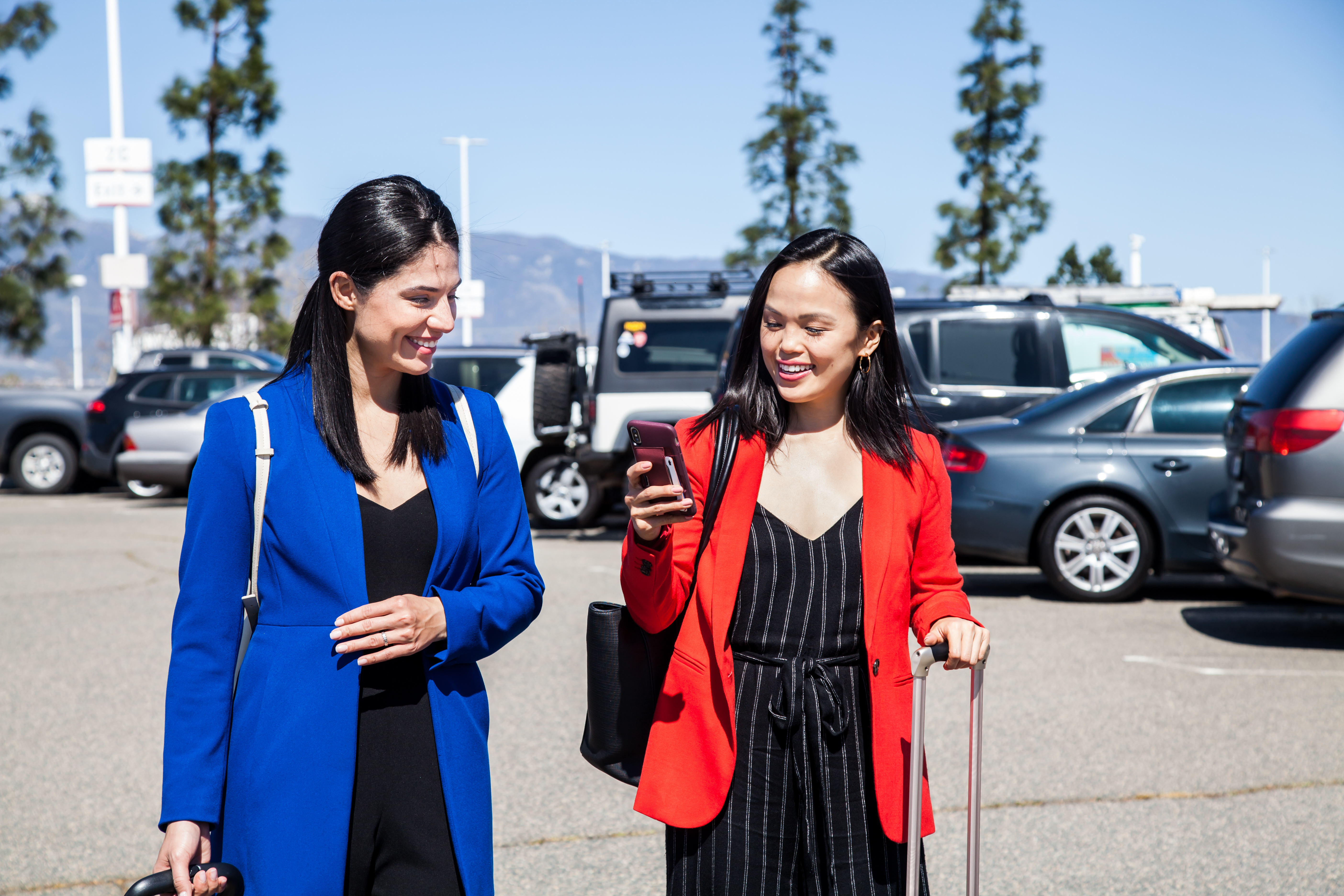 Two women walking together in a parking lot, one wearing blue and one wearing a red cardigan.