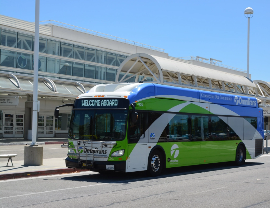 Green and silver transit bus parked at a modern airport terminal building.