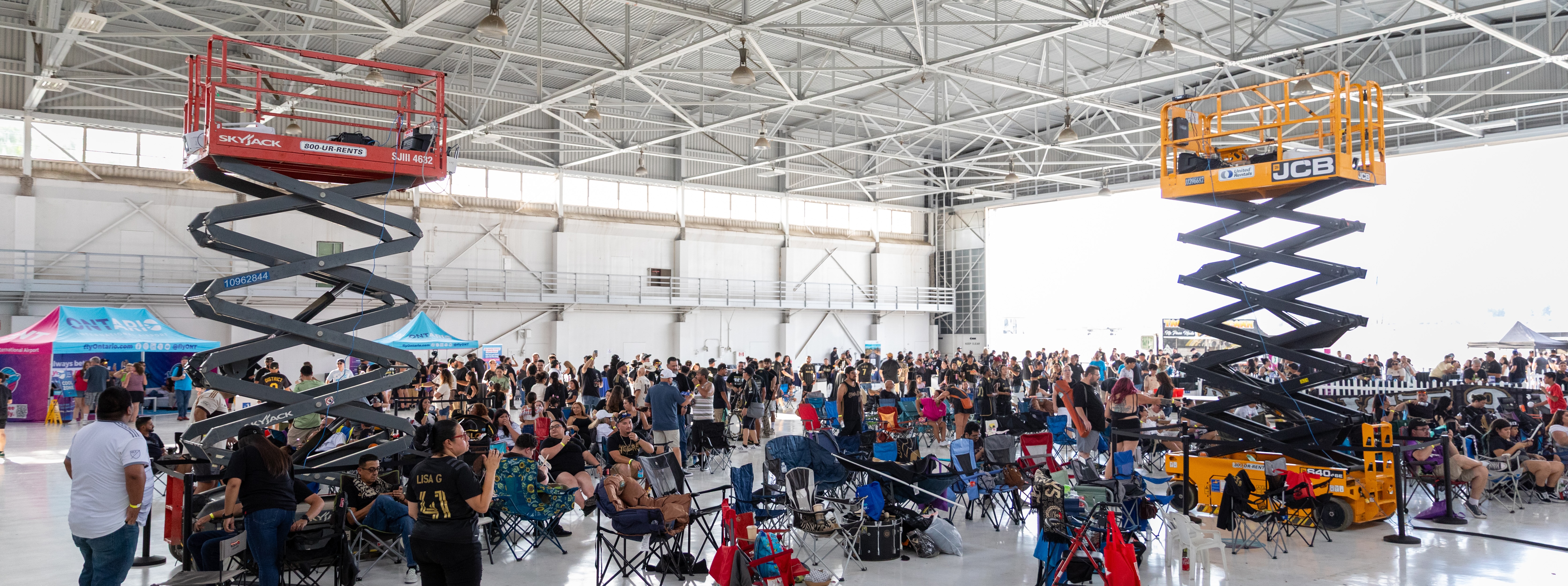 A crowded indoor event space with raised scissor lifts and exhibition displays.