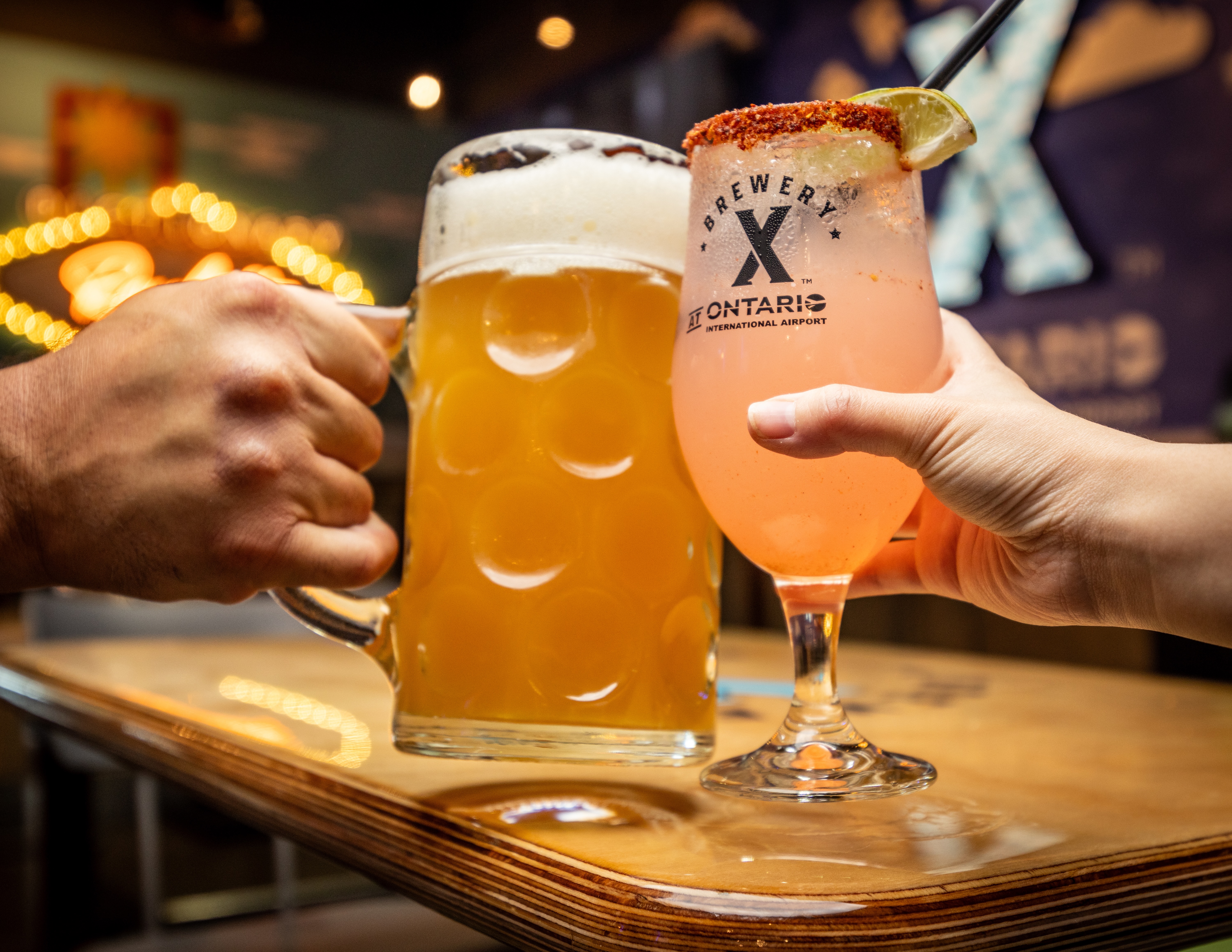 Two glasses of beer, one large mug and one stemmed glass, being toasted together on a wooden table.