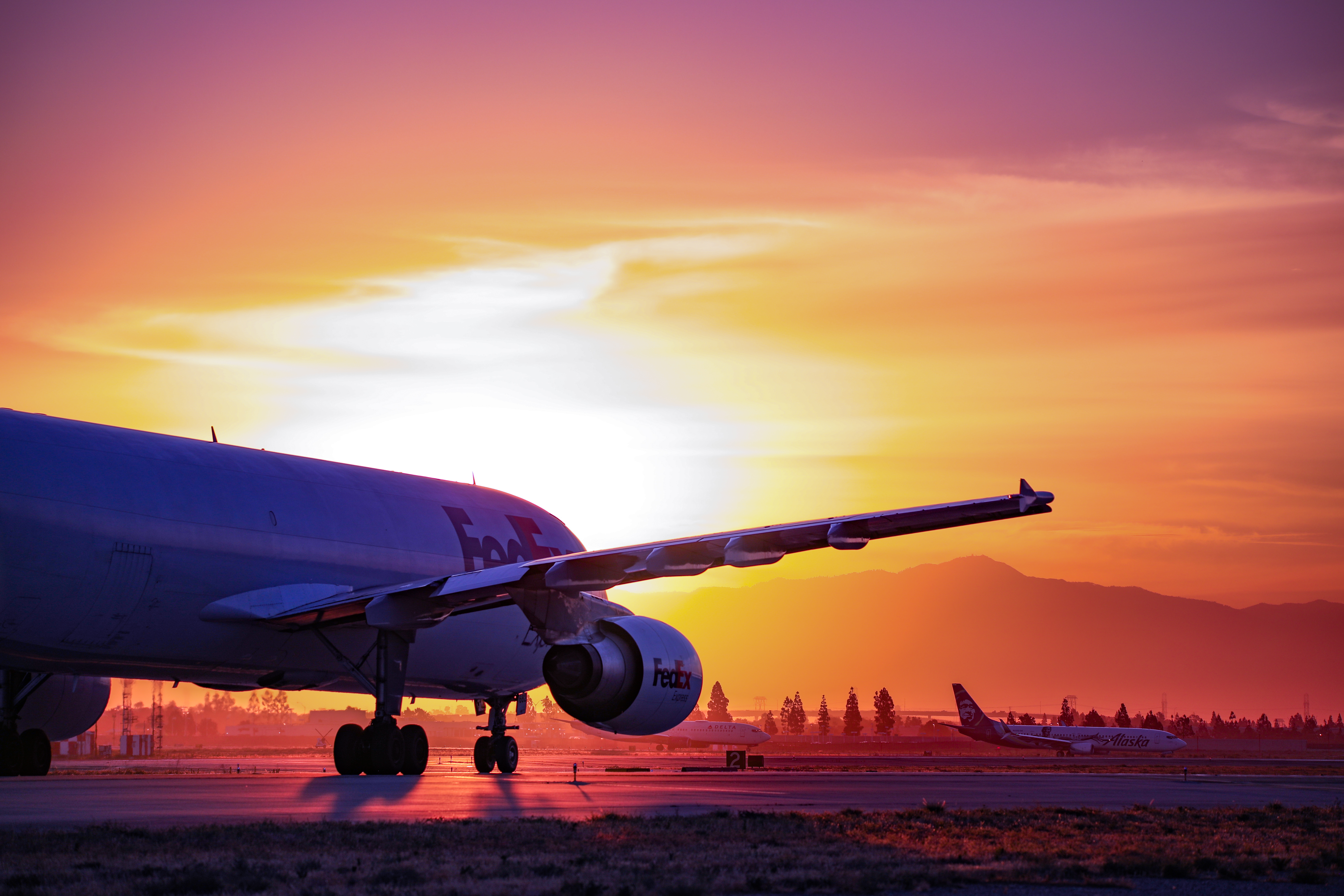 A FedEx plane sits on the ONT runway with a bright sunset behind it.