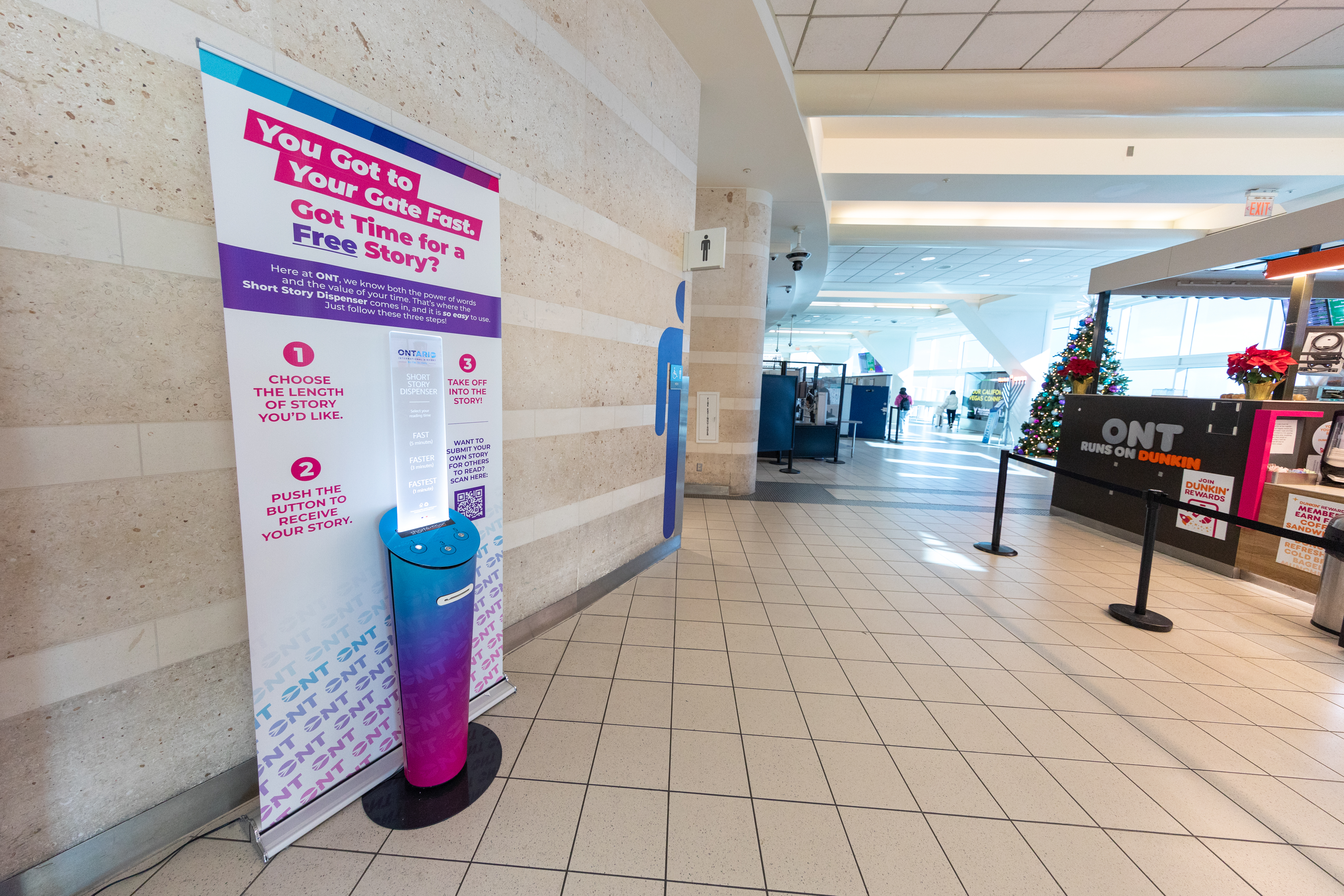 View of short story dispenser in a terminal at ONT, with a sign that says "You got to your gate fast. Got time for a free story?"