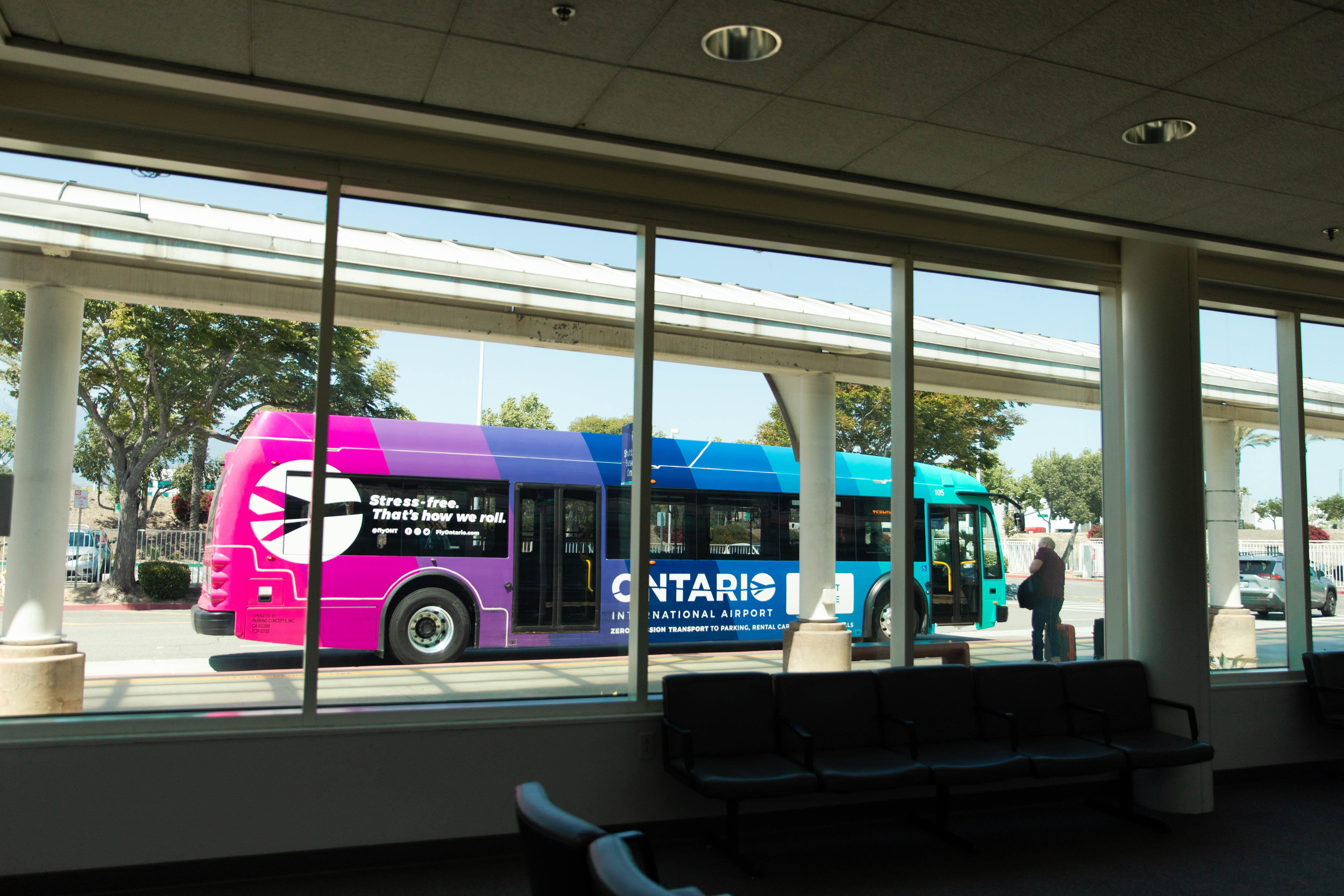 A brightly colored ONT shuttle bus is seen through the windows of an airport terminal.