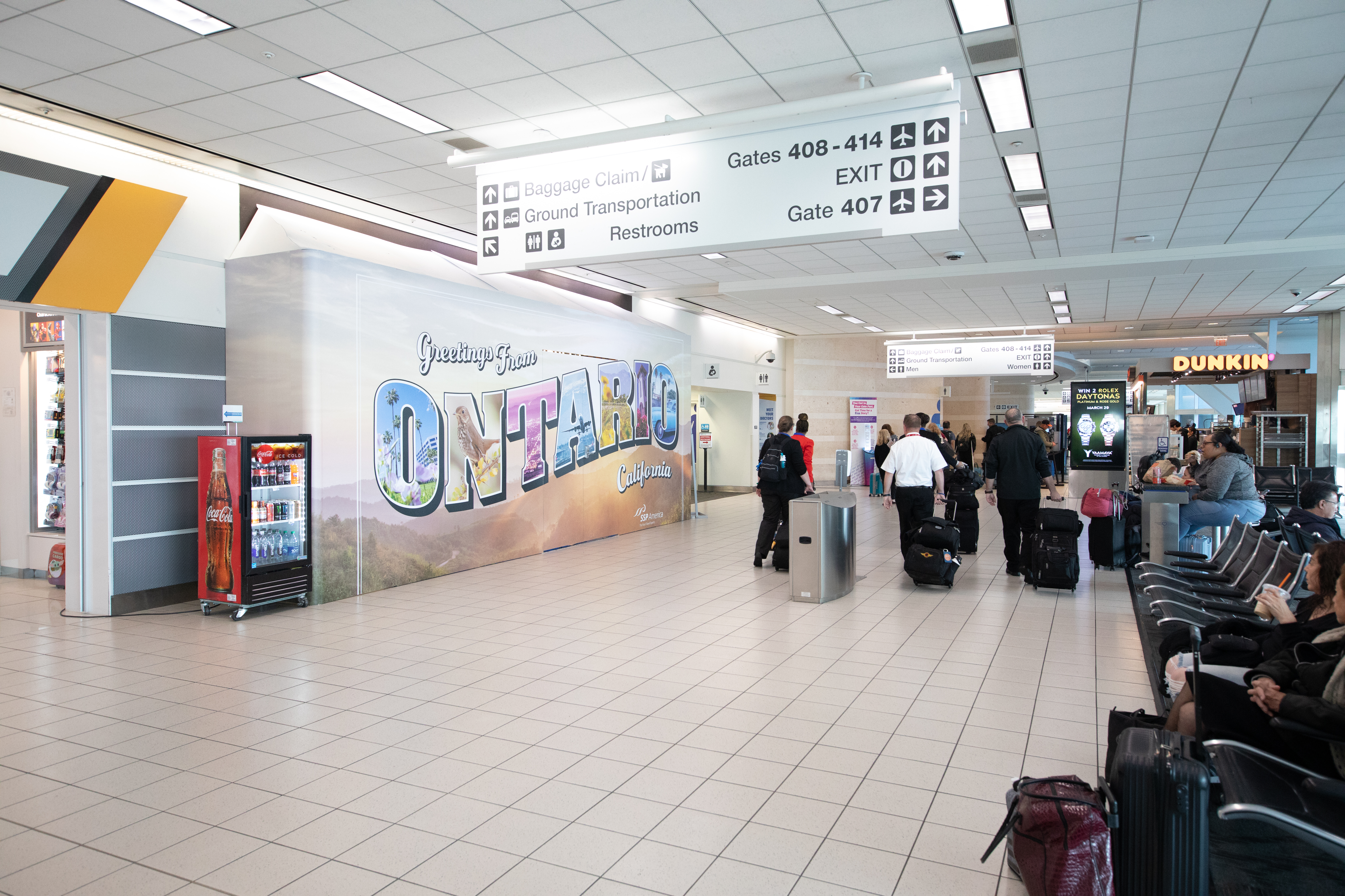 People walk through Terminal 4 pulling suitcases with a "Greetings from Ontario" mural on the wall.