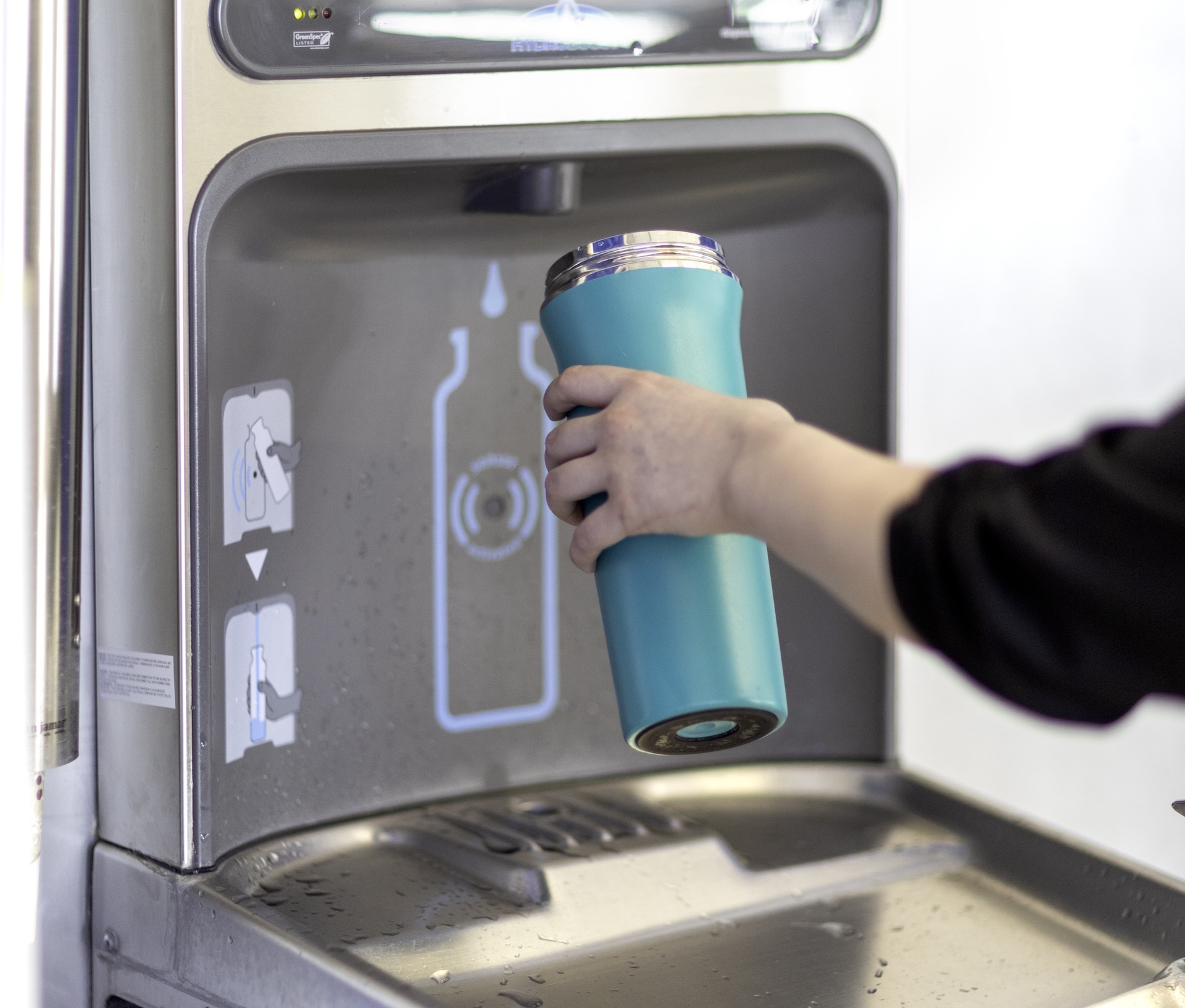 Person filling teal reusable water bottle at a water dispensing station.