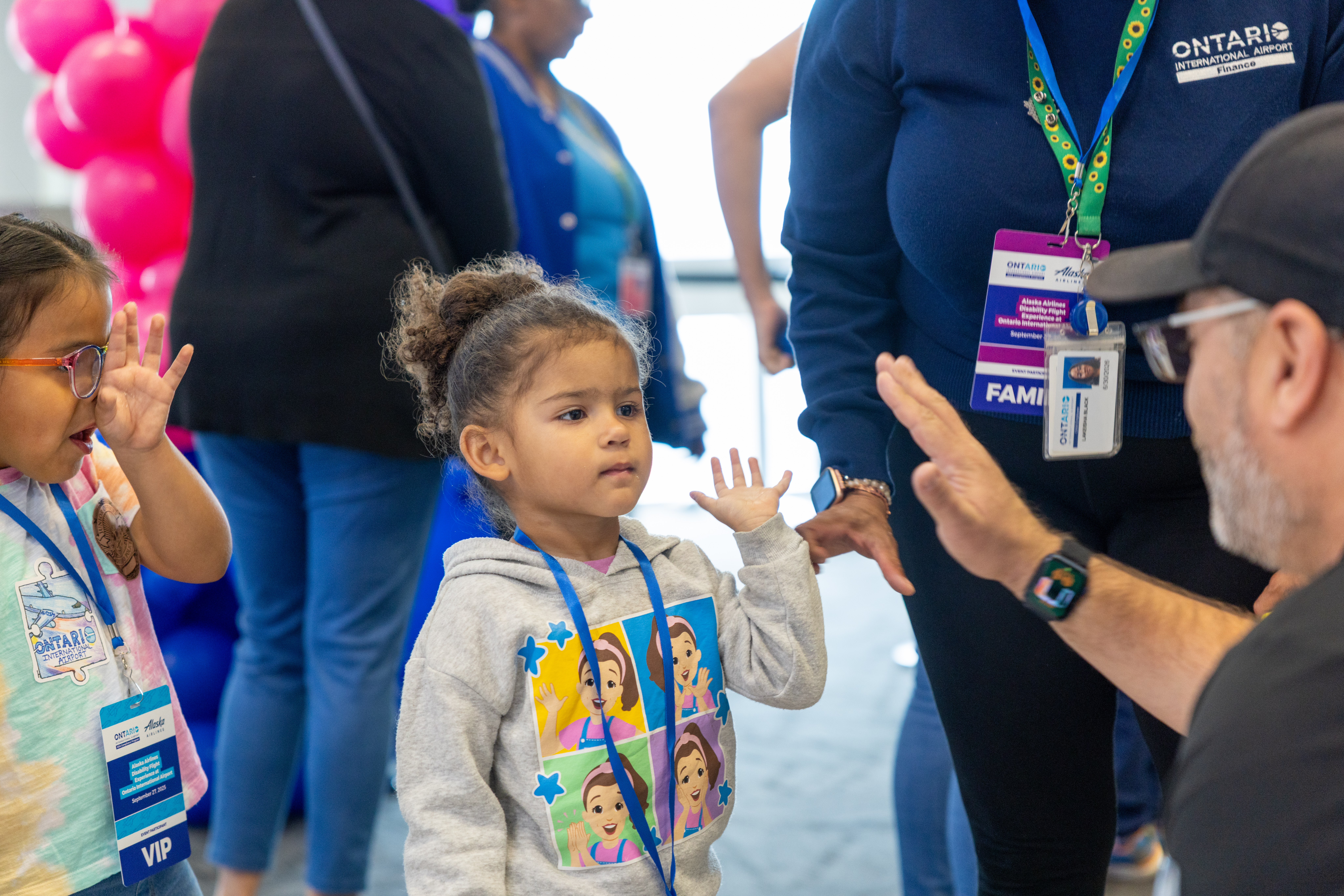 A volunteer high-fives a girl who's wearing a badge to indicate she's part of the mock flight as another girl looks on.