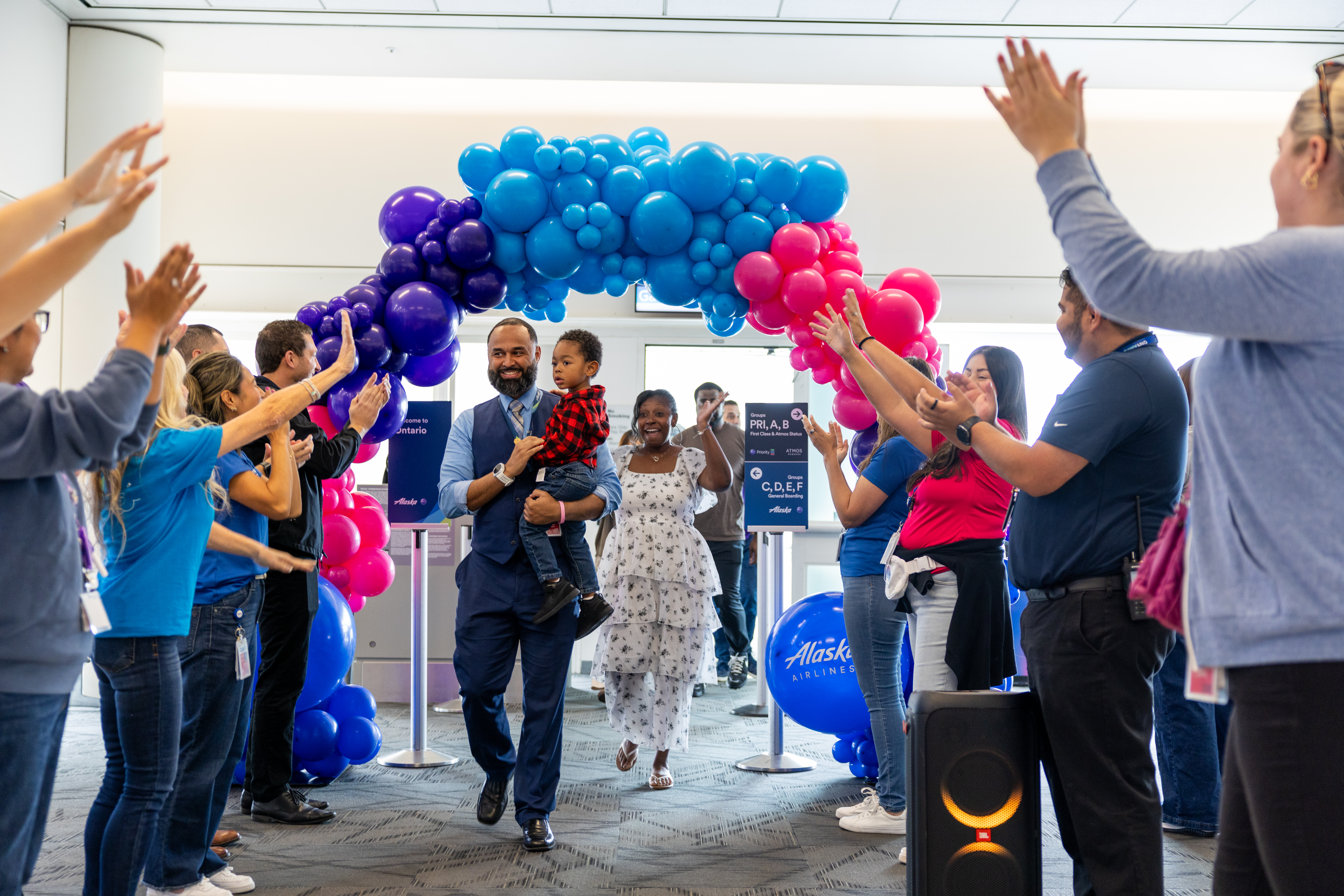 Volunteers cheer with their hands in the air as an airline worker carrying a young boy walks under a balloon arch.