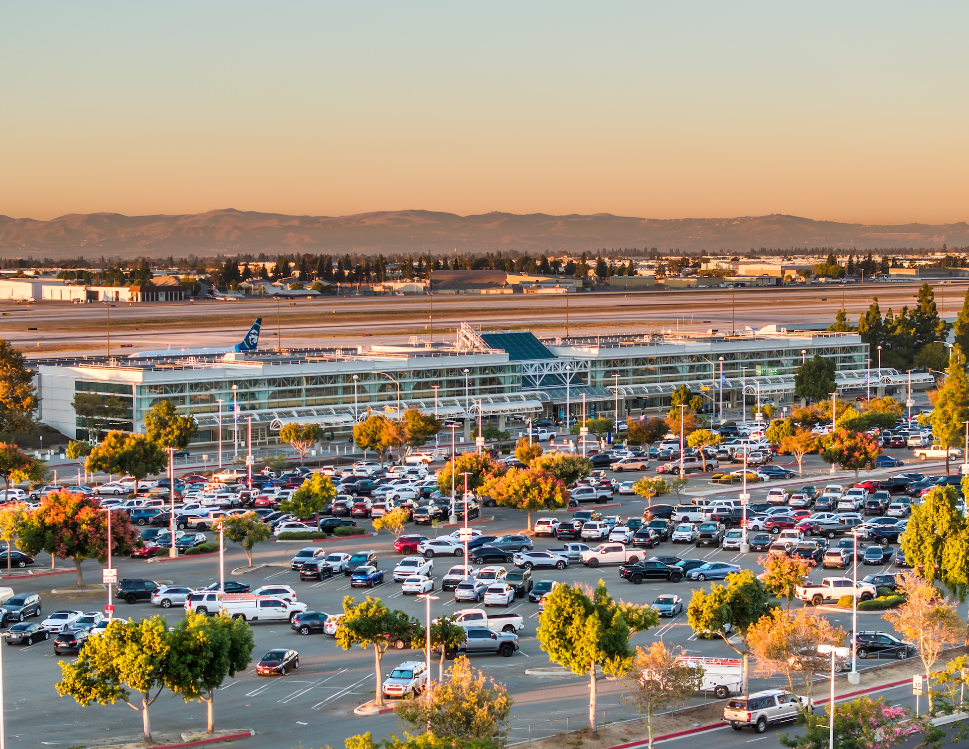 FlyONT airport exterior with parking lot at sunset, mountains visible in background.