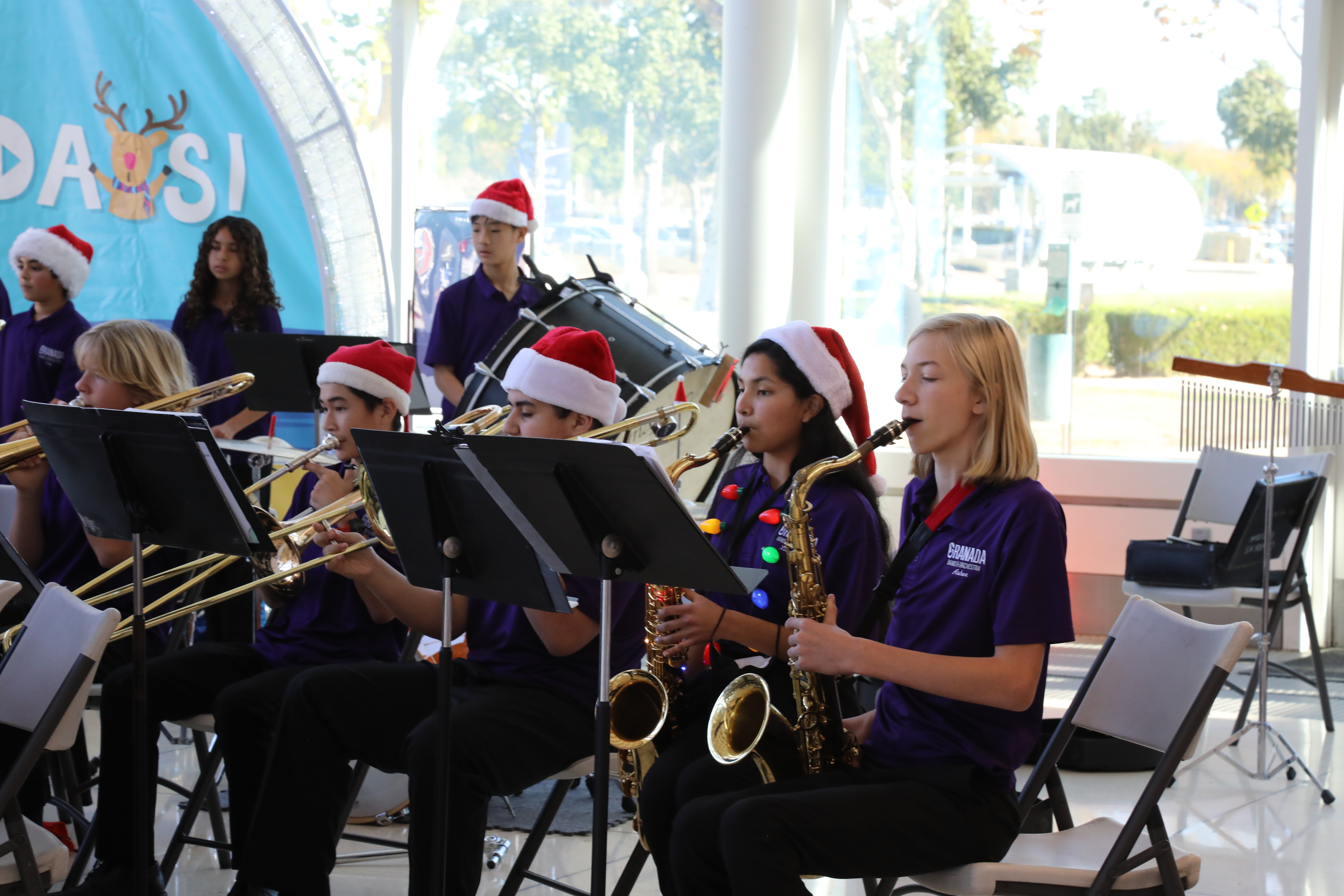 High school band students perform on horns in seats at ONT with holiday decorations behind them.