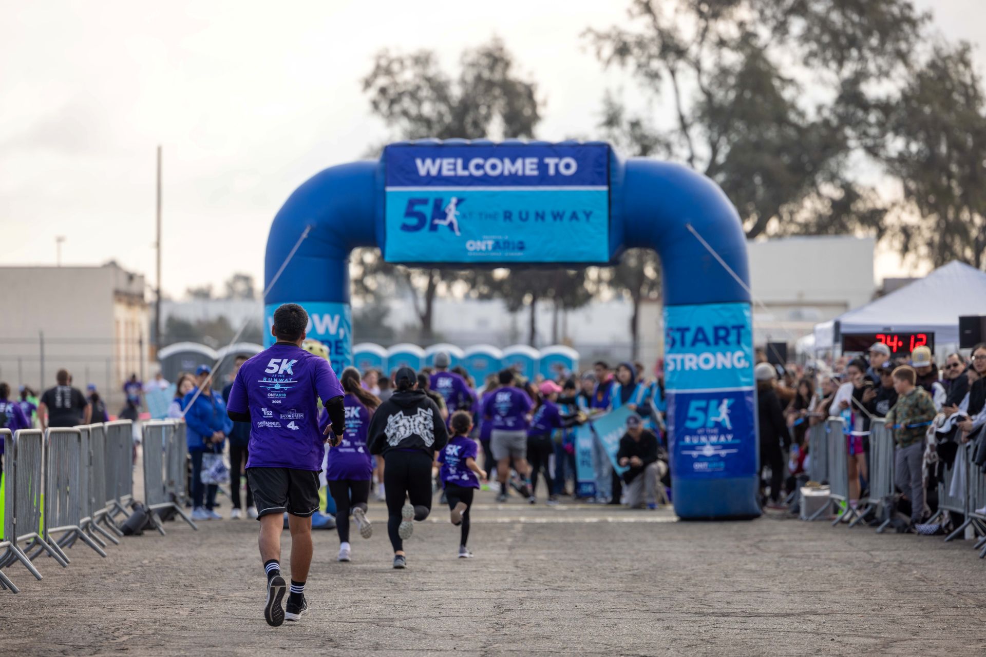 Runners wearing ONT bib numbers run under a blue, inflatable finish line as crowds look on.