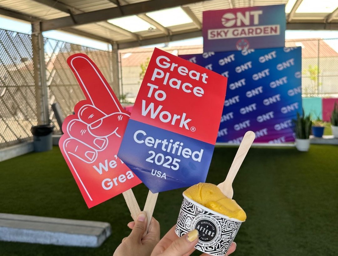 A red thumbs-up hand and a sign say ONT is a Great Place to Work with a cup of ice cream held up during a celebration.