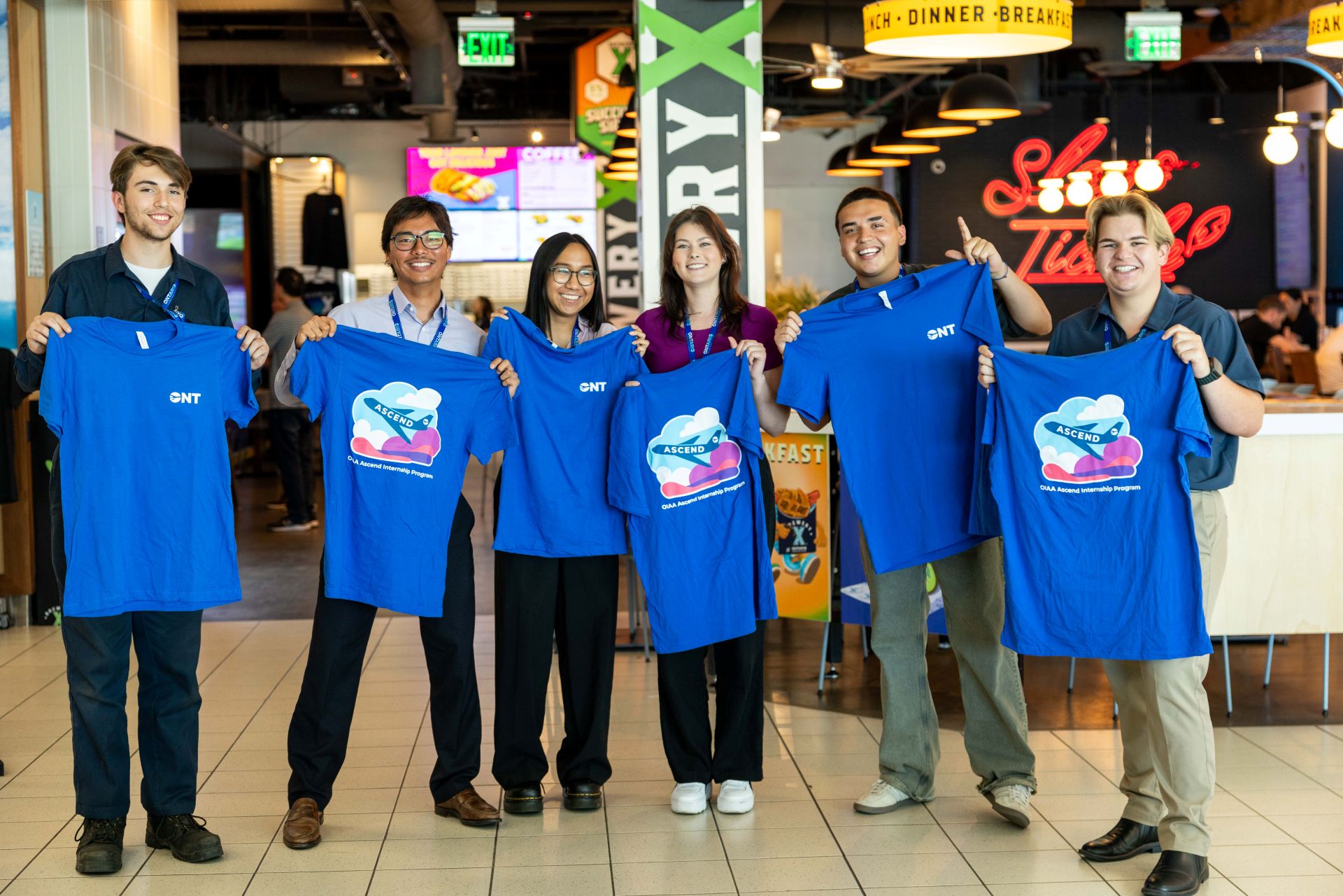 Six young people pose with blue ONT T-shirts near Brewery X at ONT.