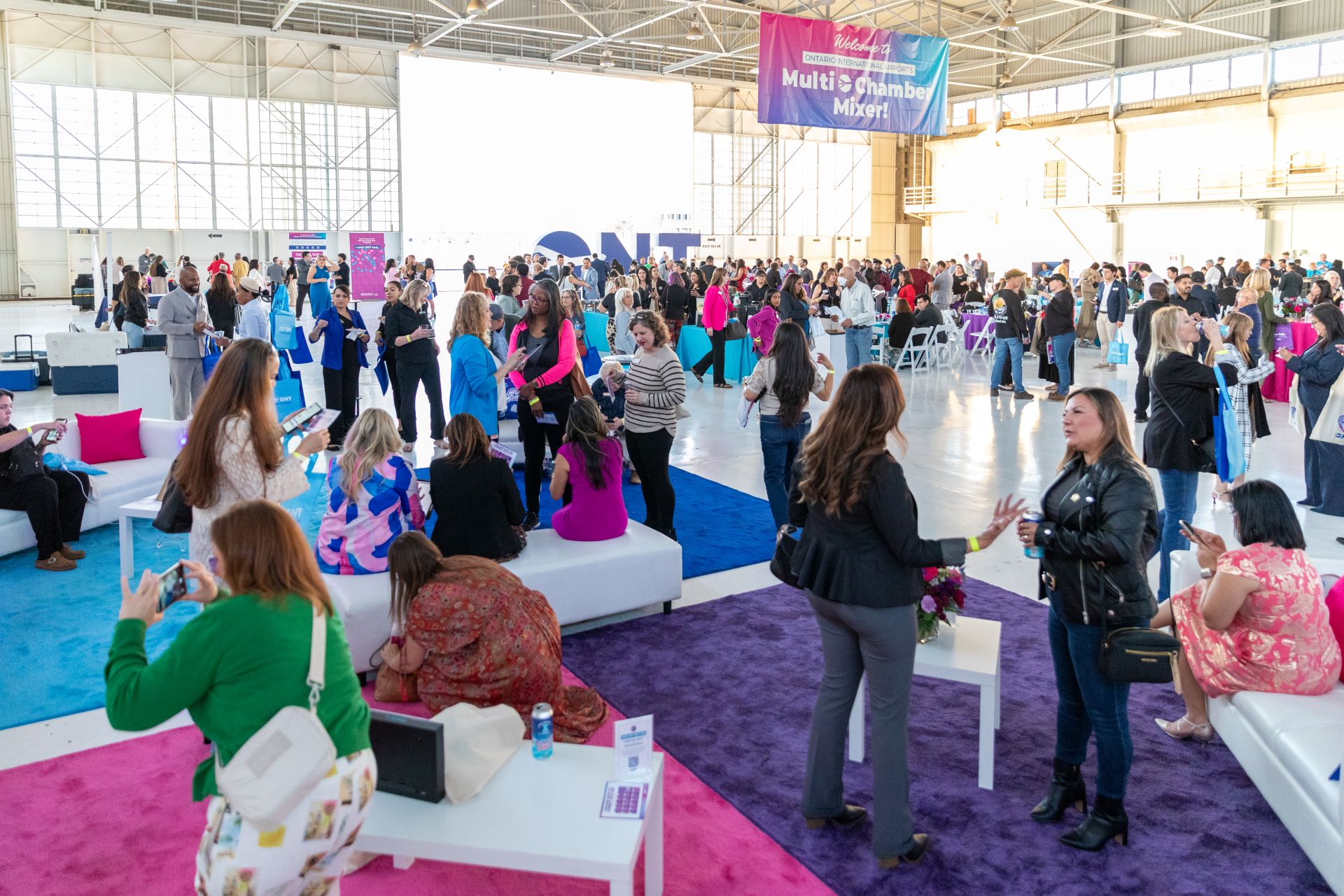 A large crowd of people network inside a hangar with ONT signs and colors all around.