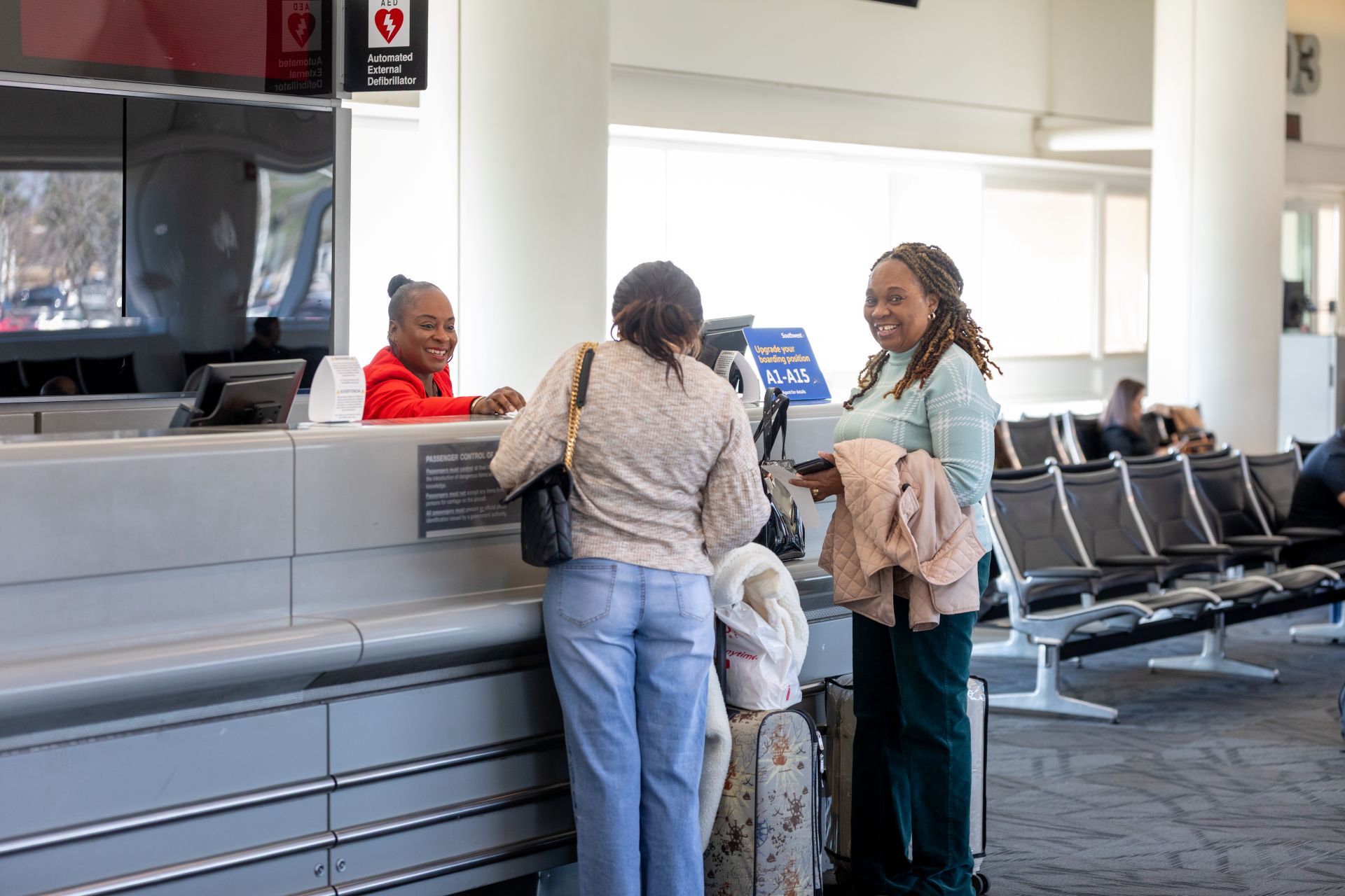 A woman at a ticket counter looks back and smiles while standing by a friend.