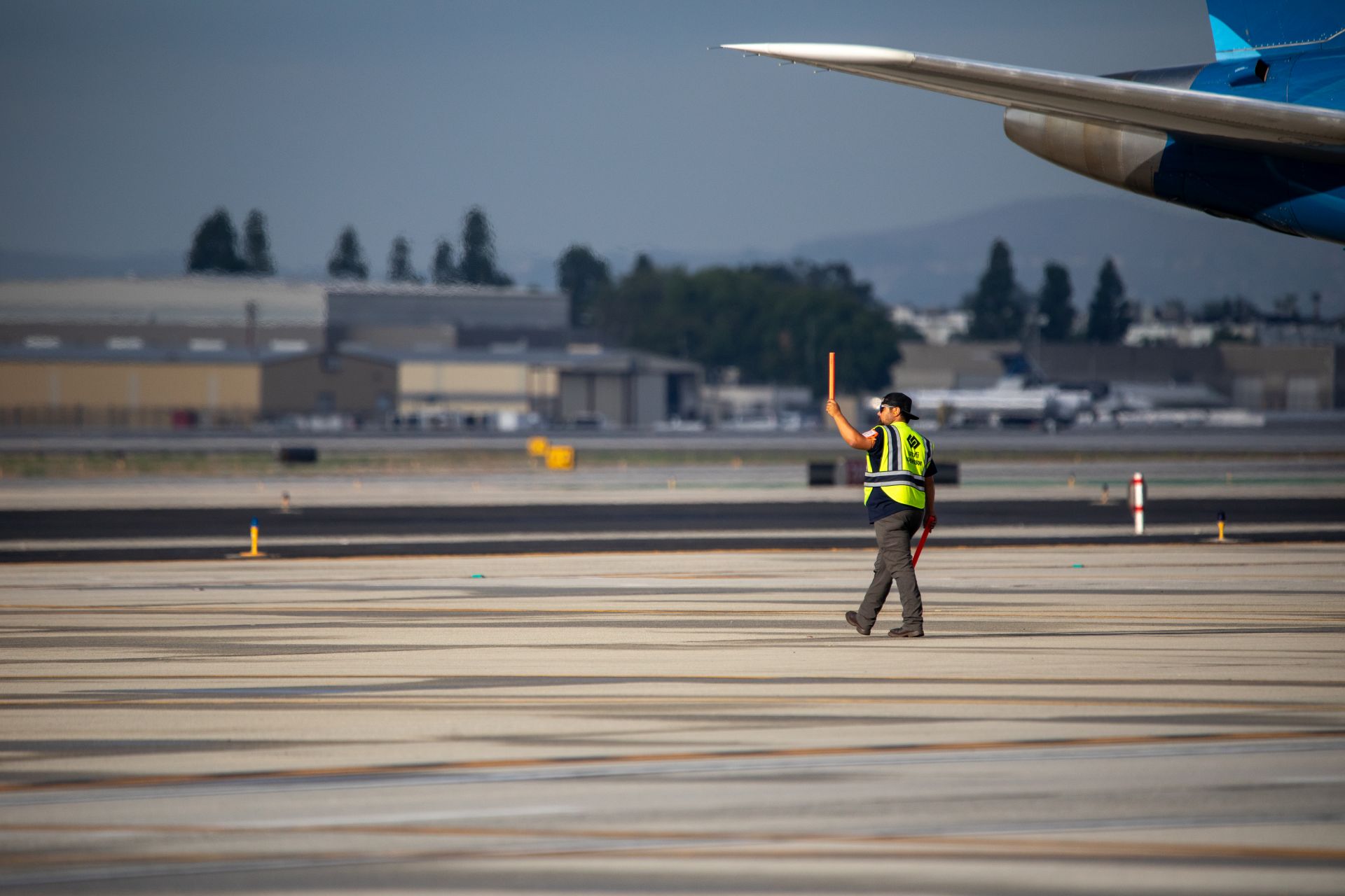 A worker waves an orange baton under the wing of a plane on the runway at ONT.