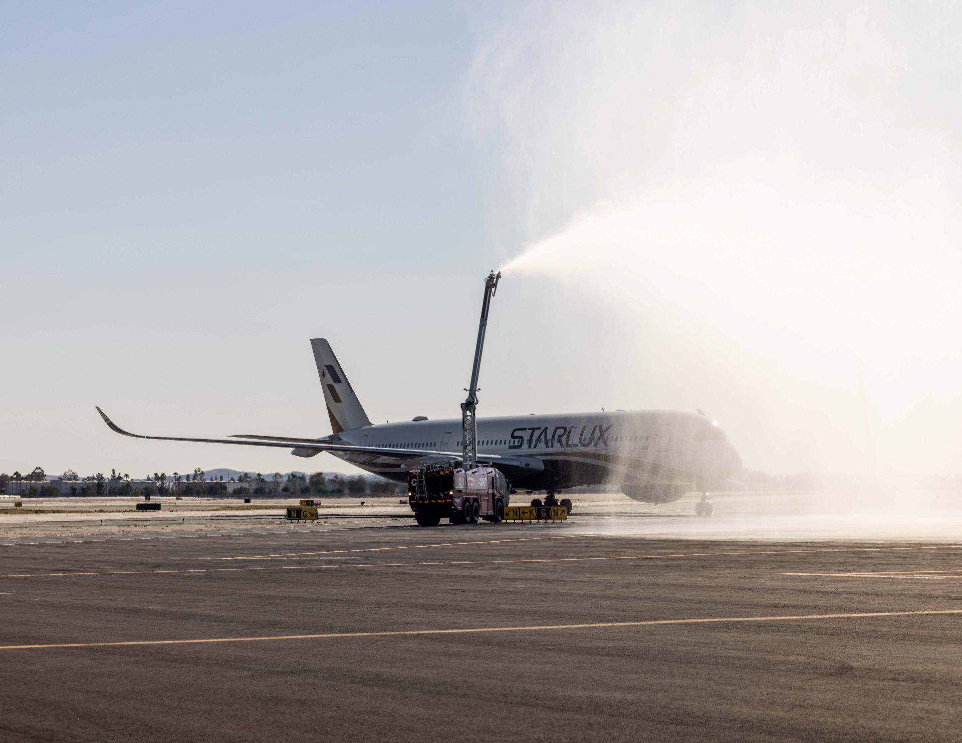 A STARLUX plane lands on the runway at ONT with water cannons shooting over it.