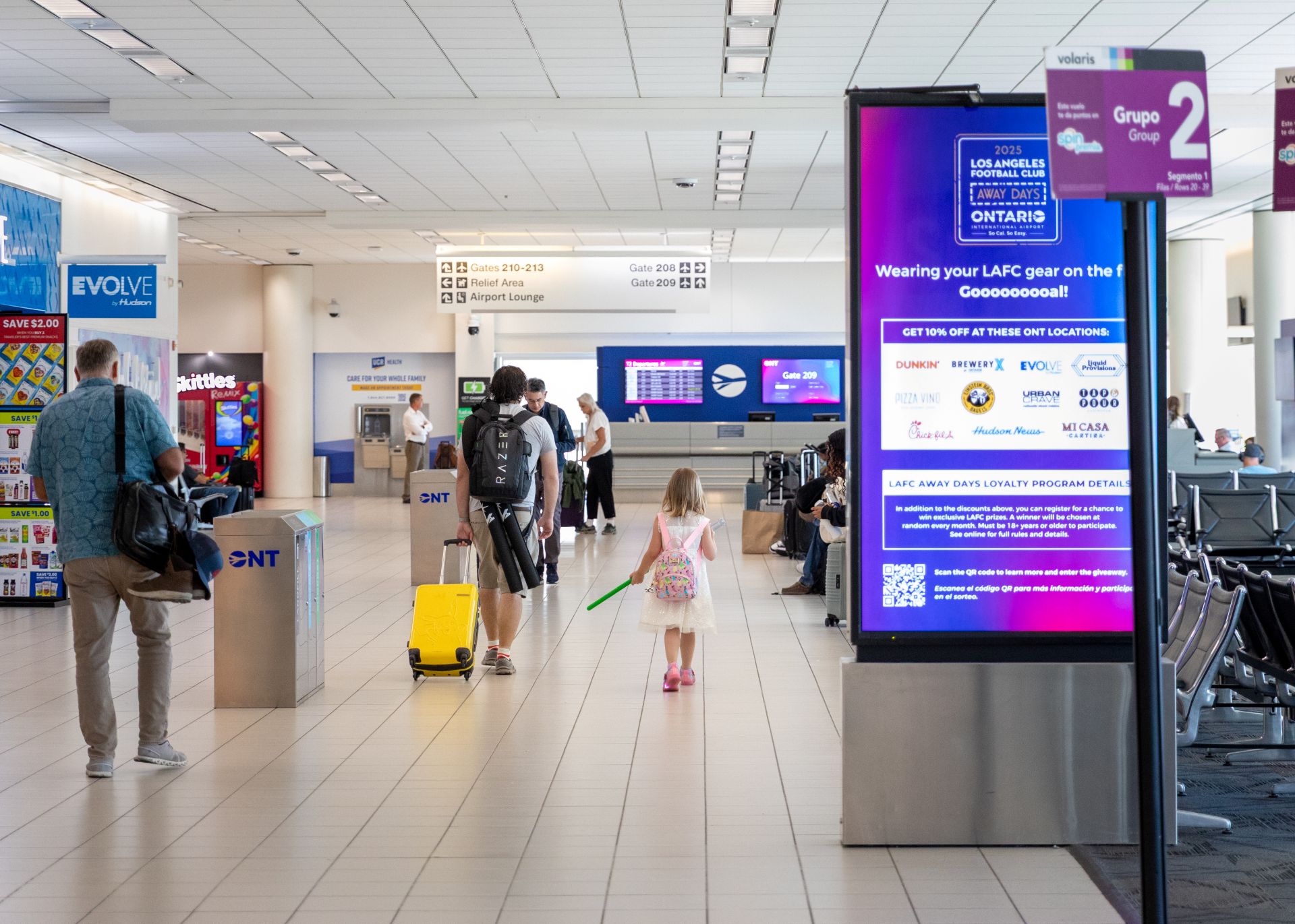 A young girl is seen walking with an adult pulling a suitcase through an ONT terminal.