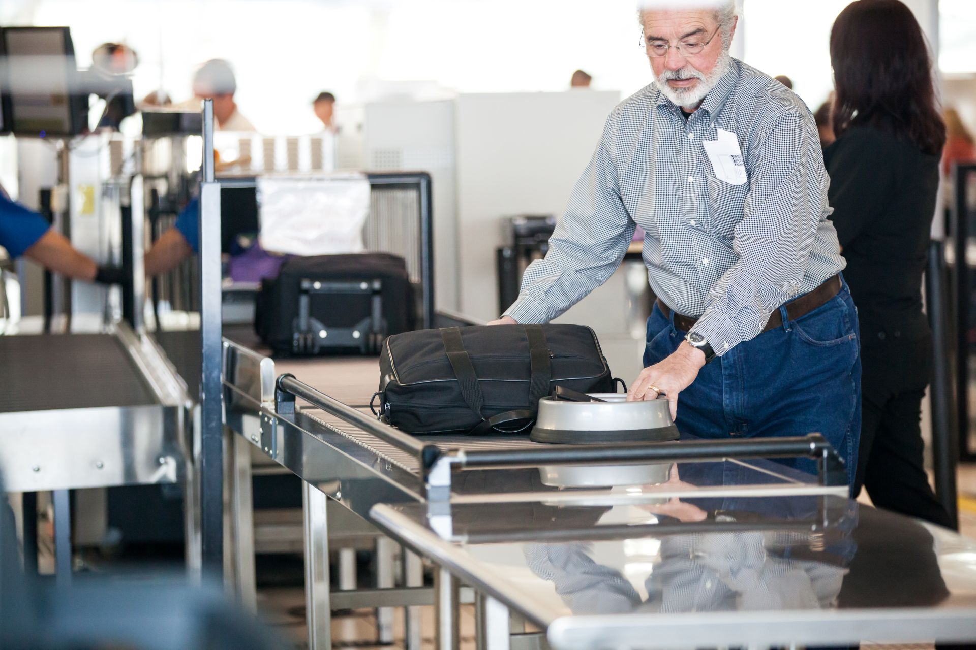 A man is shown pushing his luggage along the TSA checkpoint lane toward the scanner.