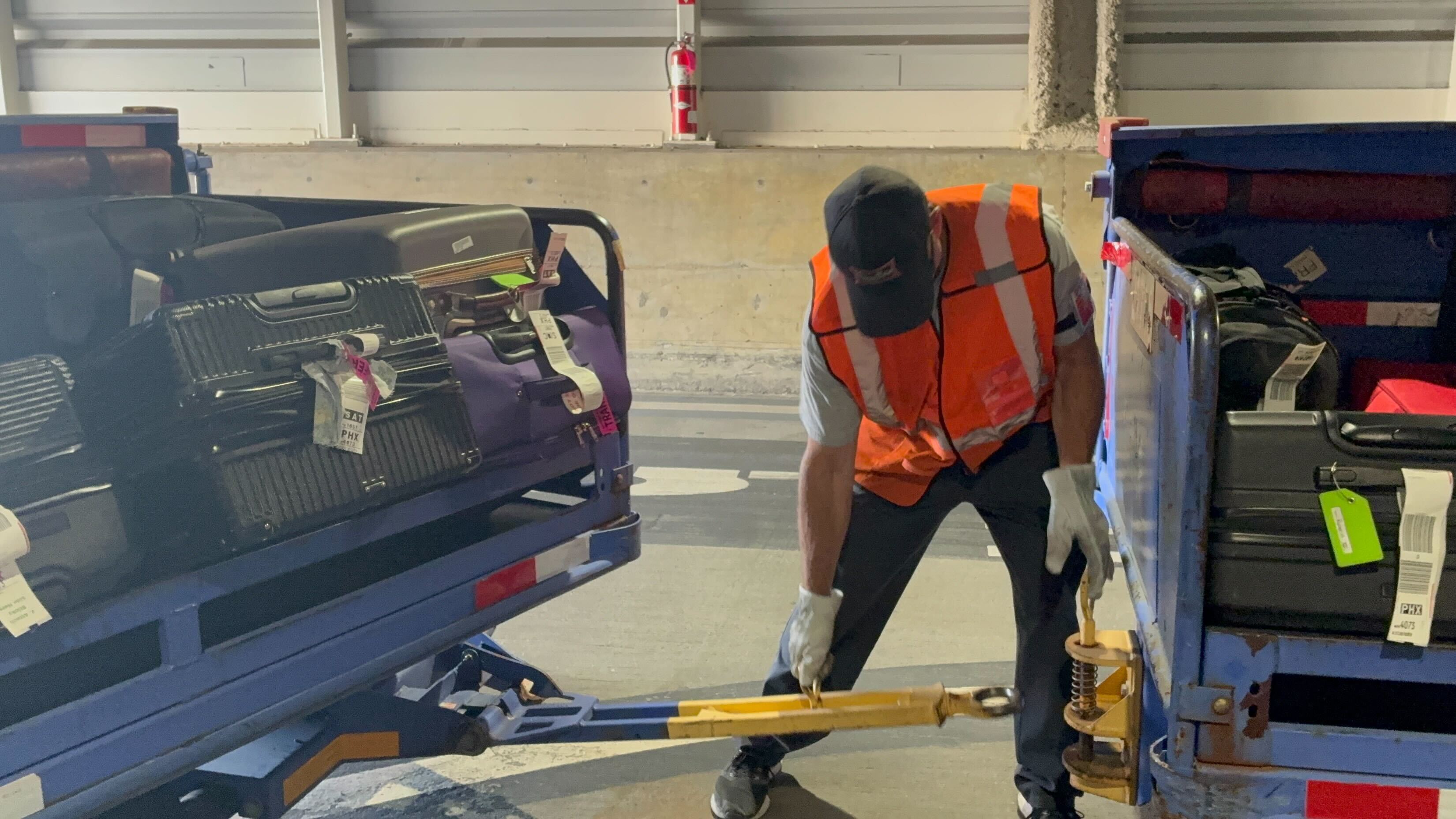 Baggage Handler tying the baggage cart to transport vehicle.