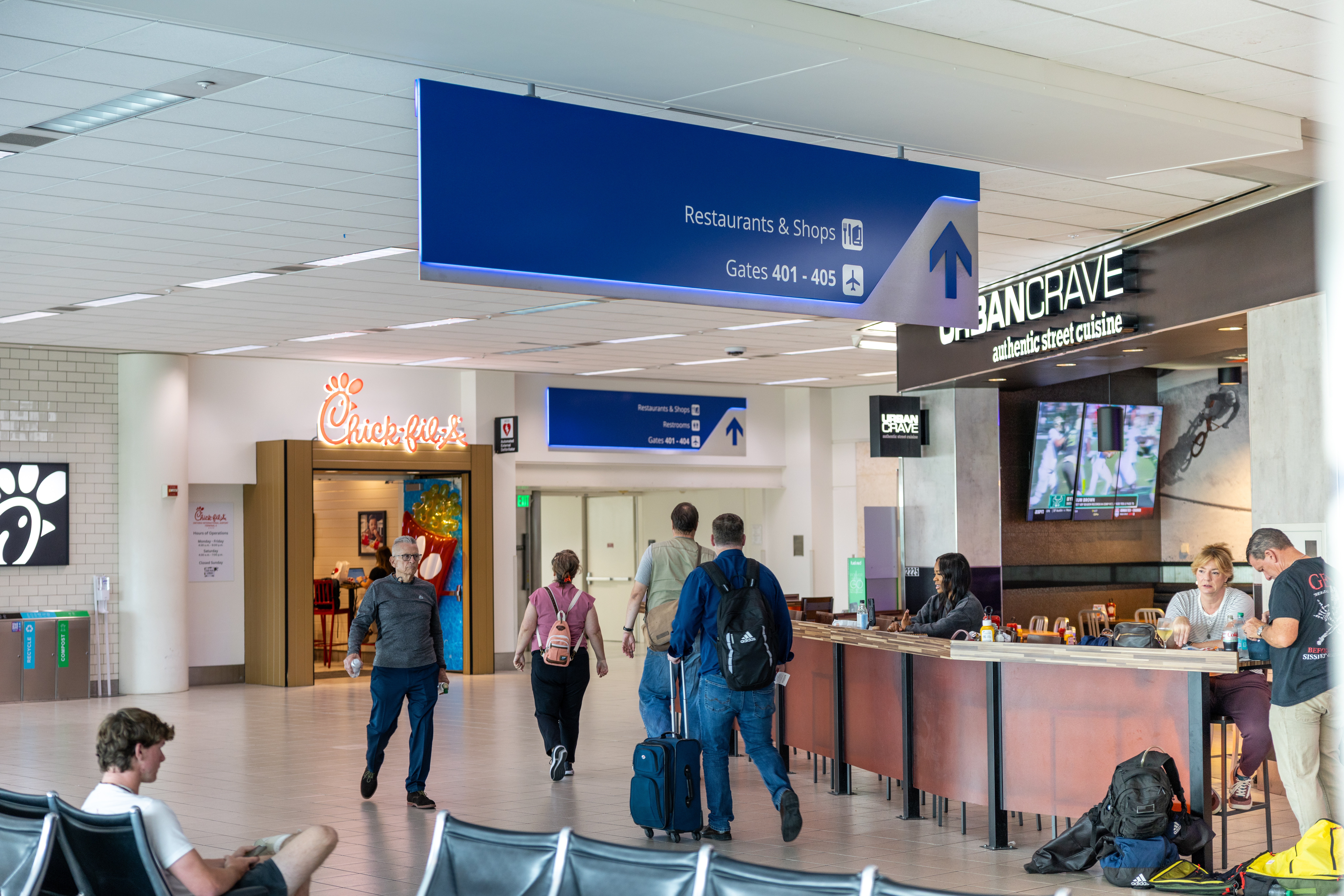 Passengers sitting down at a restaurant and walking through the terminal. 