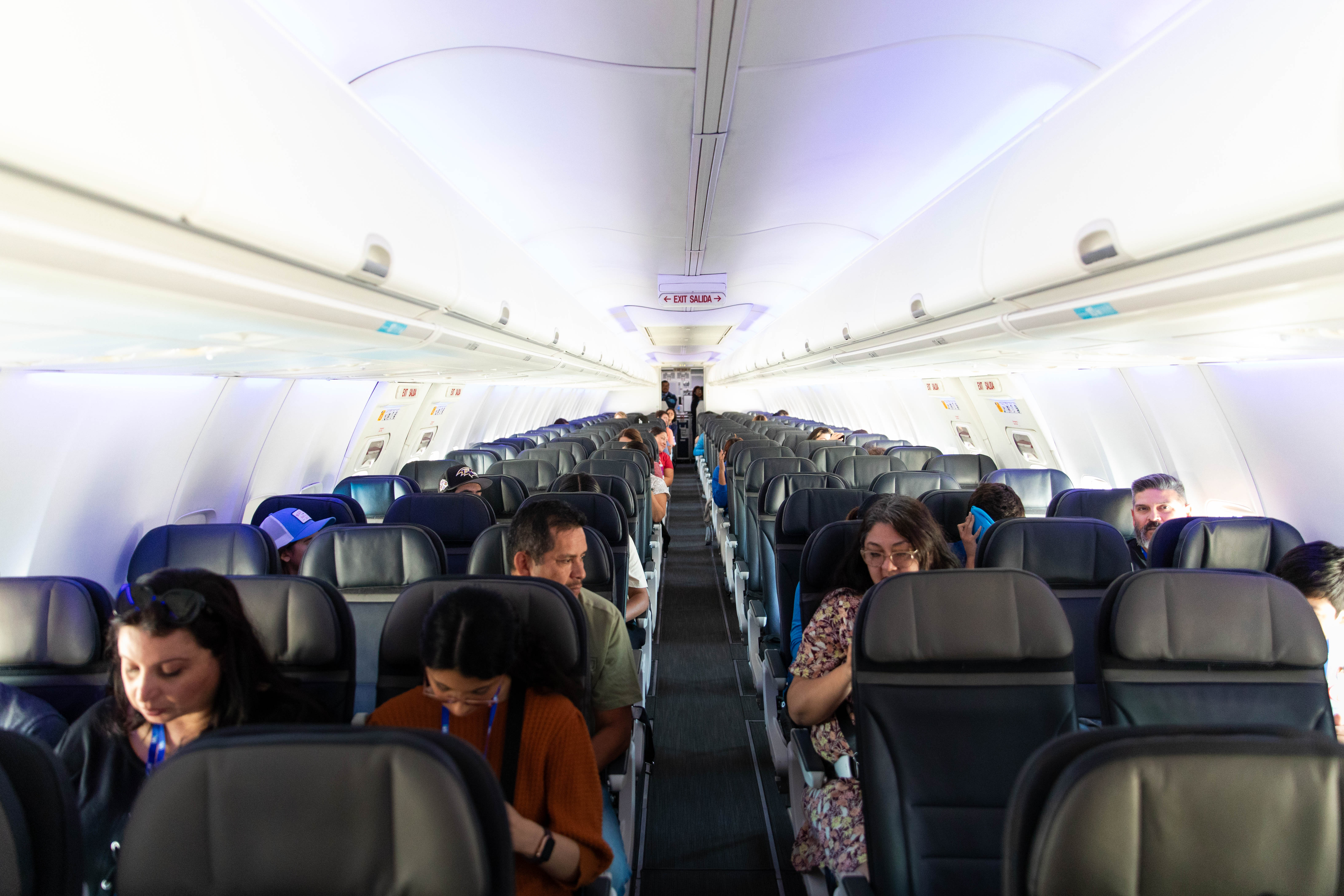 Passengers are seen sitting on an airplane and looking at devices.