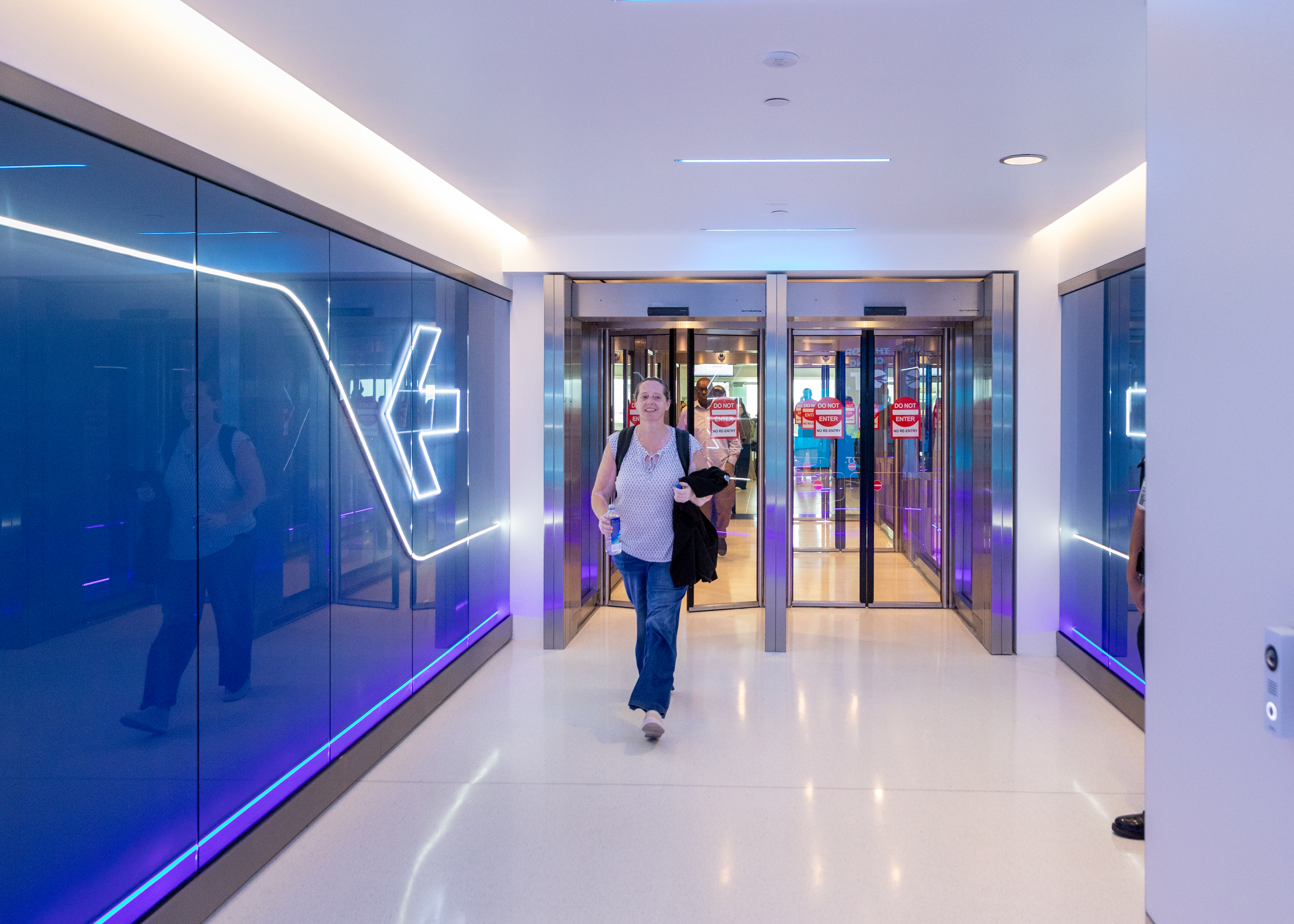 Modern exit corridor with blue glass walls and people walking through.