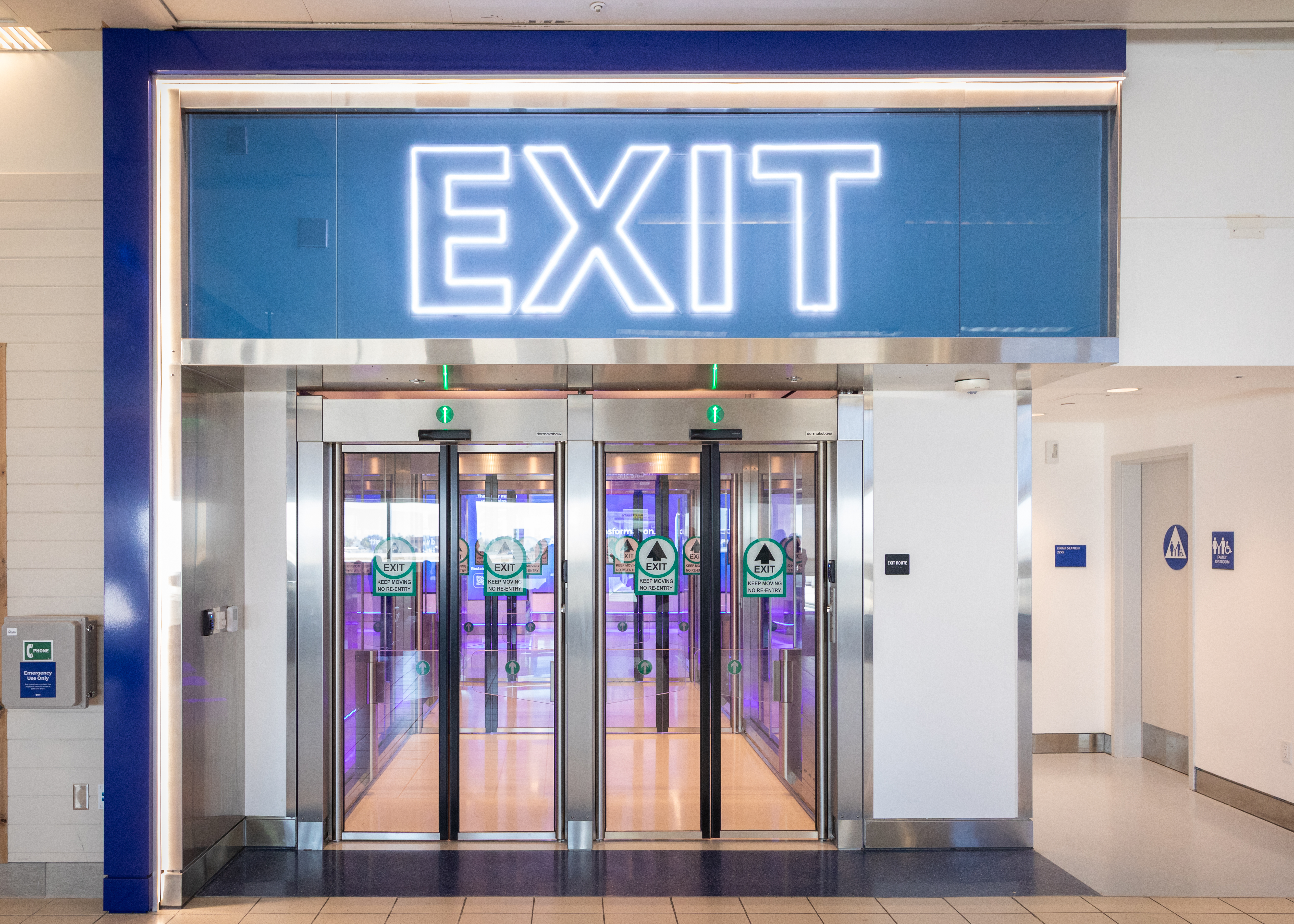 Glass doors beneath illuminated blue EXIT sign in modern building interior