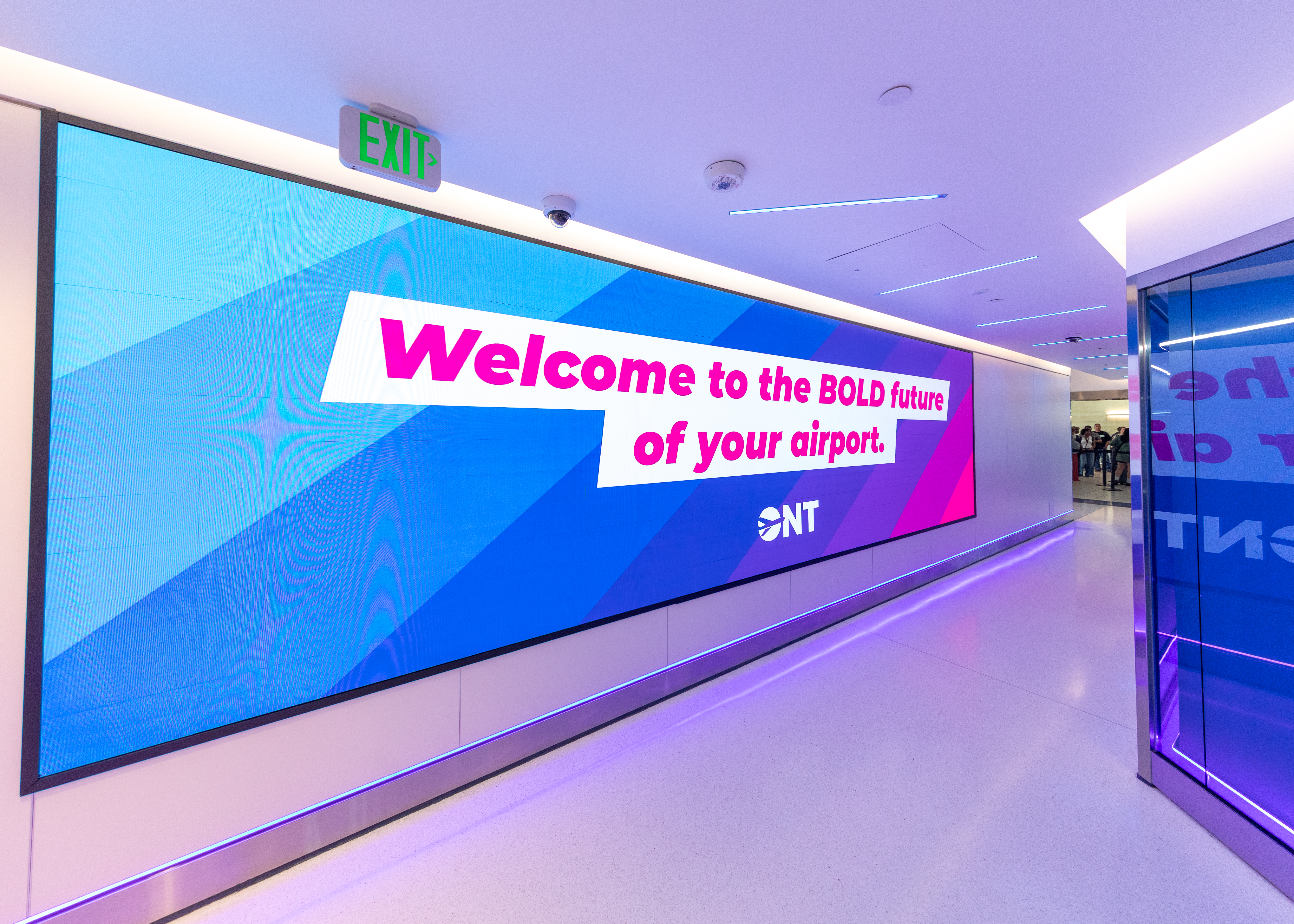 Modern airport corridor with purple lighting and digital welcome sign
