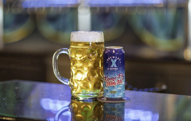Photo of mug next to an branded aluminum can of the Come Fly With Me beer. 