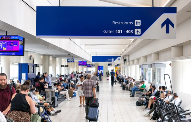 Busy airport terminal with passengers waiting and walking, departure signs above.