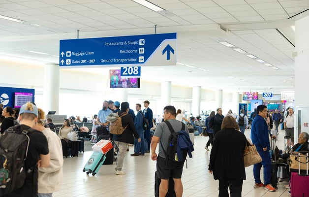 Airport terminal with travelers walking near blue directional signs and gates