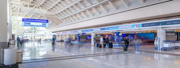 Modern airport terminal with white ceiling, blue information displays, and passenger check-in counters.