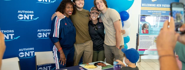 Olympian Jackie Joyner-Kersee poses for a photo with three passengers in front of a table with her children's book on display.