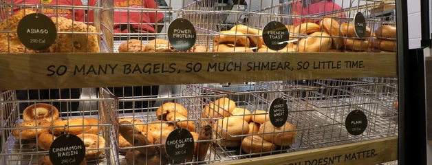 Rows of different kinds of bagels are shown in cases on shelfs.