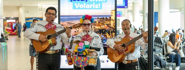 Three mariachi players perform in front of a sign that says "Welcome Los Cabos (SJD) with Volaris!"