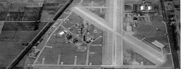 An aerial black-and-white photo shows a small runway surrounded by farm land.