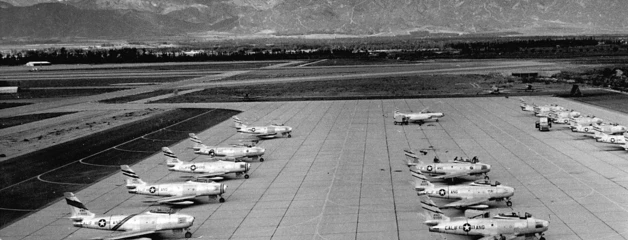 Lines of military planes are shown on the runway in front of the San Gabriel Mountains in this black-and-white photo.
