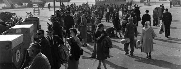 Passengers are shown walking toward planes on the runway in a black-and-white photo.