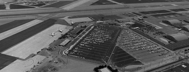 An aerial black-and-white photo of ONT shows a few plans on the tarmac and rows of cars in the parking lot.