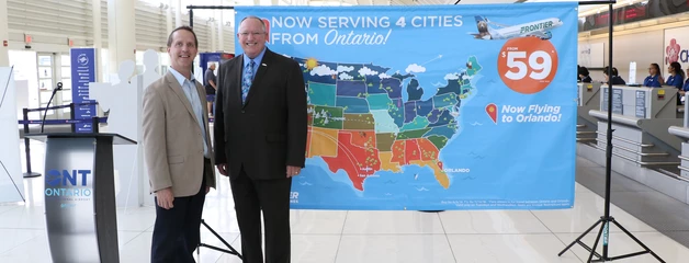 Frontier and ONT leaders pose in the terminal in front of a sign about new routes launching at ONT.