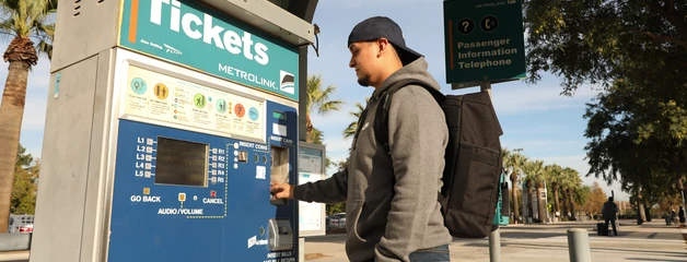 A man wearing a black backpack buys a train ticket.