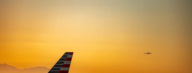 Airplane tail silhouetted against a golden sunset sky with mountains in the distance.