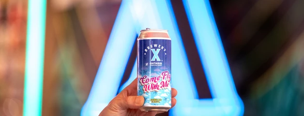 A can of BX beer against blue neon lighting in a bar or venue.