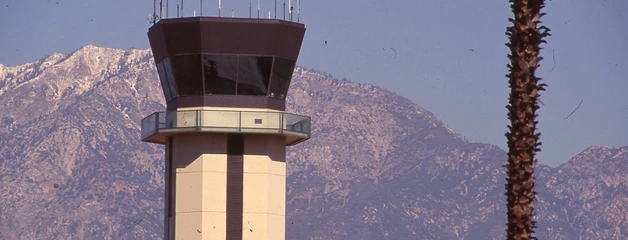 The Air Traffic Control tower is shown near a palm tree with the San Gabriel Mountains in the background.
