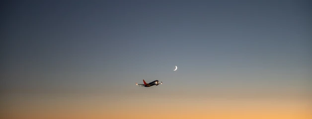 A plane towards the sunset with a sliver of moon in the distance.
