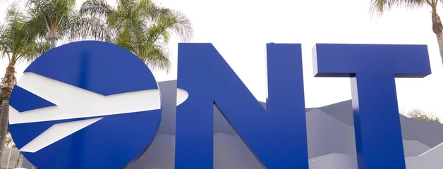 Big blue letters spell ONT with a white plane cutting through the O and mountains behind on a sign at the airport with grass in front of it.