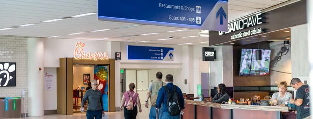 Passengers sitting down at a restaurant and walking through the terminal. 