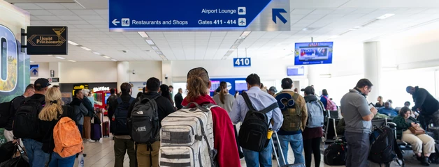 Crowded airport gate with passengers waiting to board, blue overhead signage