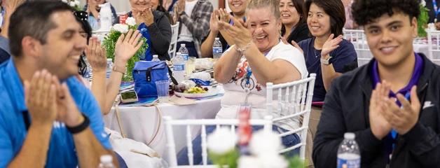Employees sitting at tables smiling and clapping. 